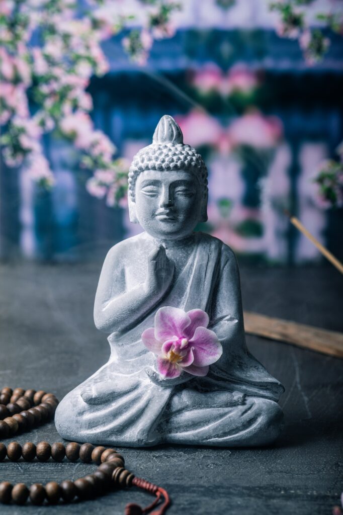 stone statue of buddha on a stone window sill surrounded by flowers and smoke asian celebrations